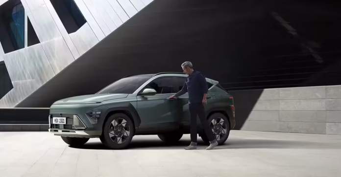 kona-hibrido-porta.avif Homem de camisa azul abrindo a porta do motorista do Novo Kona Hybrid estacionado durante o dia.