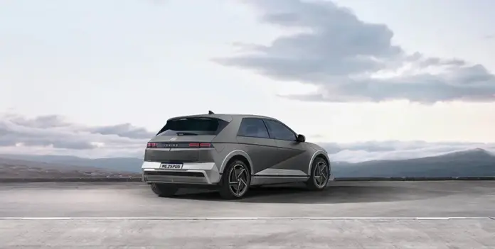 Visão traseira do modelo IONIQ 5 na cor cinza estacionado de dia com montanhas ao fundo.